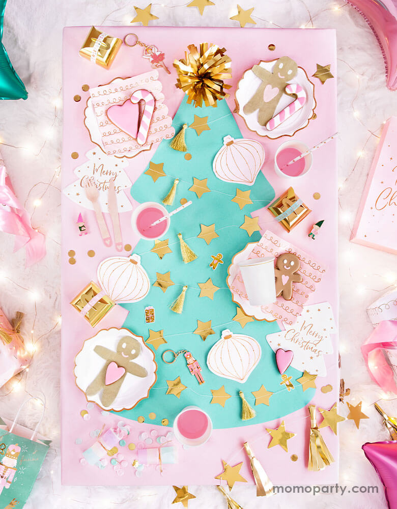 An adorable pastel Christmas themed party table filled with Party Deco's pink Christmas tableware including gingerbread man napkins, Christmas ornament napkins, pastel colored confetti and gold star banners on a mint Christmas tree shaped table runner