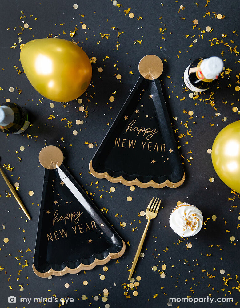 New Year's Eve countdown party table filled with Momopartys's 10 x 7 inches Happy New Year Hat Shaped Plates by My Mindy's Eye, featuring black and gold foil accents, with the message of "Happy New Year", gold confetti, gold forks and gold latex balloon and champagne.