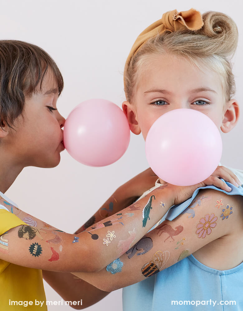 Boy and girl play bubble gum and holding each other's shoulder with full of fun temporary Tattoos on their arms