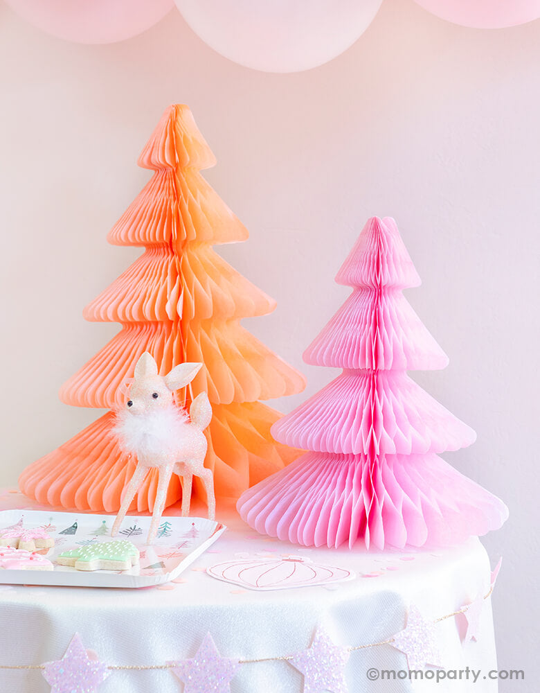 Pastel Pink Christmas party table set up with Devra Party Peach and light pink Honeycomb Paper Christmas Trees, a cute deer ornament decoration, Fa la la christmas tree plate with tree cookies on a kid table, and pastel matt pink balloons as decoration