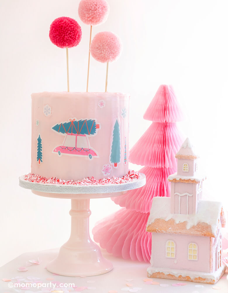 Momo-Party-Holiday Set up with Pastel pink buttercream cake decorated with Let's Get A Tree! Cakescape Edible Stickers of christmas tree on a truck, snowflakes stickers. Cake By Courtney Pom Pom Cake Toppers, , Peppermint Crush Candies. Light Pink Honeycomb Paper Christmas Tree, a snow pink house decoration on the table for a modern cute sweet cozy look holiday celebration