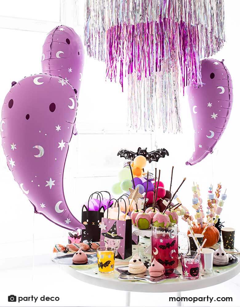 Party Deco 14 inches pink ghost foil balloons featuring iridescent moon and star icons with a party table filled with Halloween party tableware including plates, cups, napkins featuring witches, black cats. bats and ghosts and Halloween treats and sweets, with a fringe silver and pink party garlands in the back, perfect for a not-so-scary kid-friendly pink Halloween party
