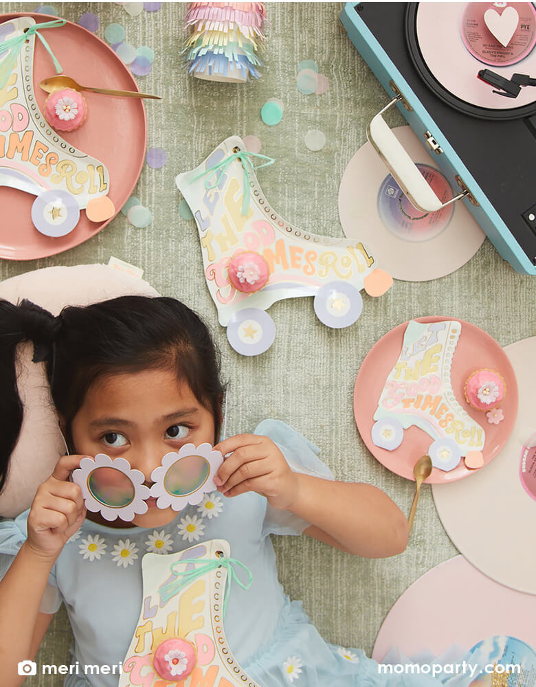 A little girl wearing a white daisy shaped sunglasses lying on the ground with some retro roller skates and a vintage record player with Momopartys's Roller Skate shaped Party tablewares including napkins, plates and party cups around. With pastel confetti spread across, this makes a festive scene for a retro inspired celebration for kids!