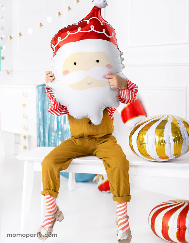 Kids Christmas Party Ideas by Momopartys featuring Party deco's 24" Santa head foil balloon held by a little girl sitting on a festive table with Christmas decorations around her