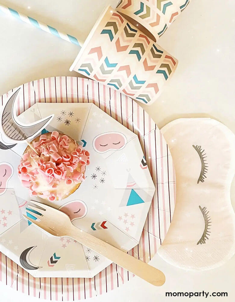 A tablescape of girls sleepover party featuring Momopartys's sleepover napkins in the shape of sleeping masks by Pooka Party, pink striped plates and light pink party cups with chevron design, perfect for girl's slumber party.