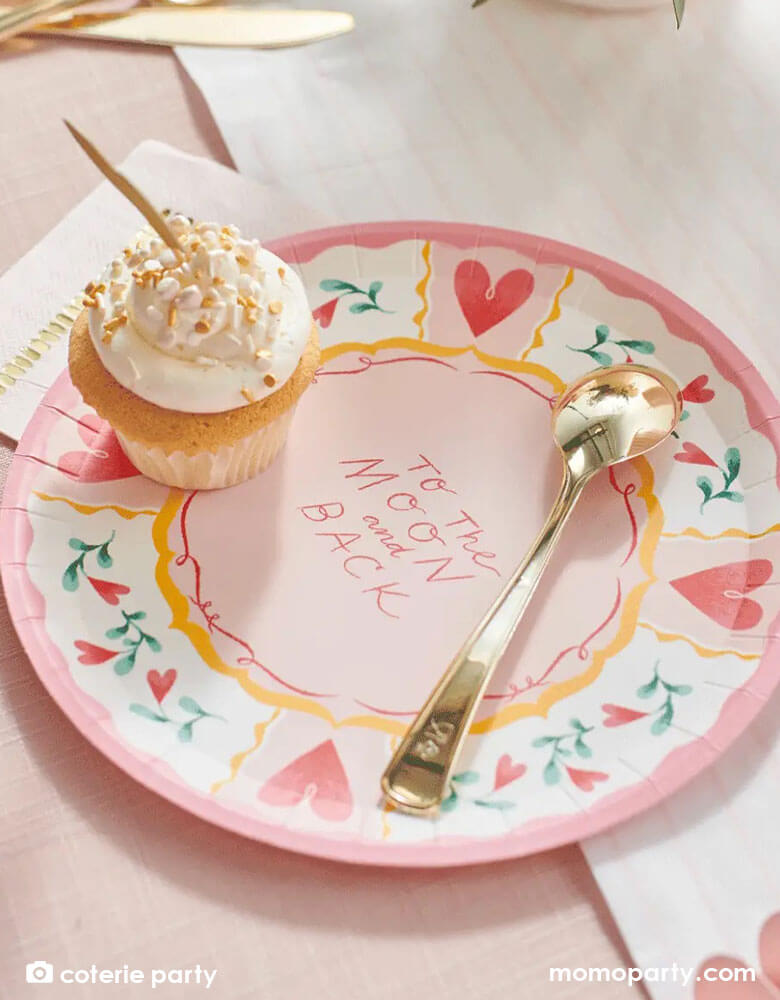 A beautiful love themed party table featuring Momopartys's 9 oz pale pink pinstripe party cups by Coterie Party and 9" All You Need is Love Large Plates with a message of "To the moon and back" on the plate. With a table set with pastel pink themed tableware with heart shaped elements, it's a perfect inspiration for a Valentine's Day celebration.