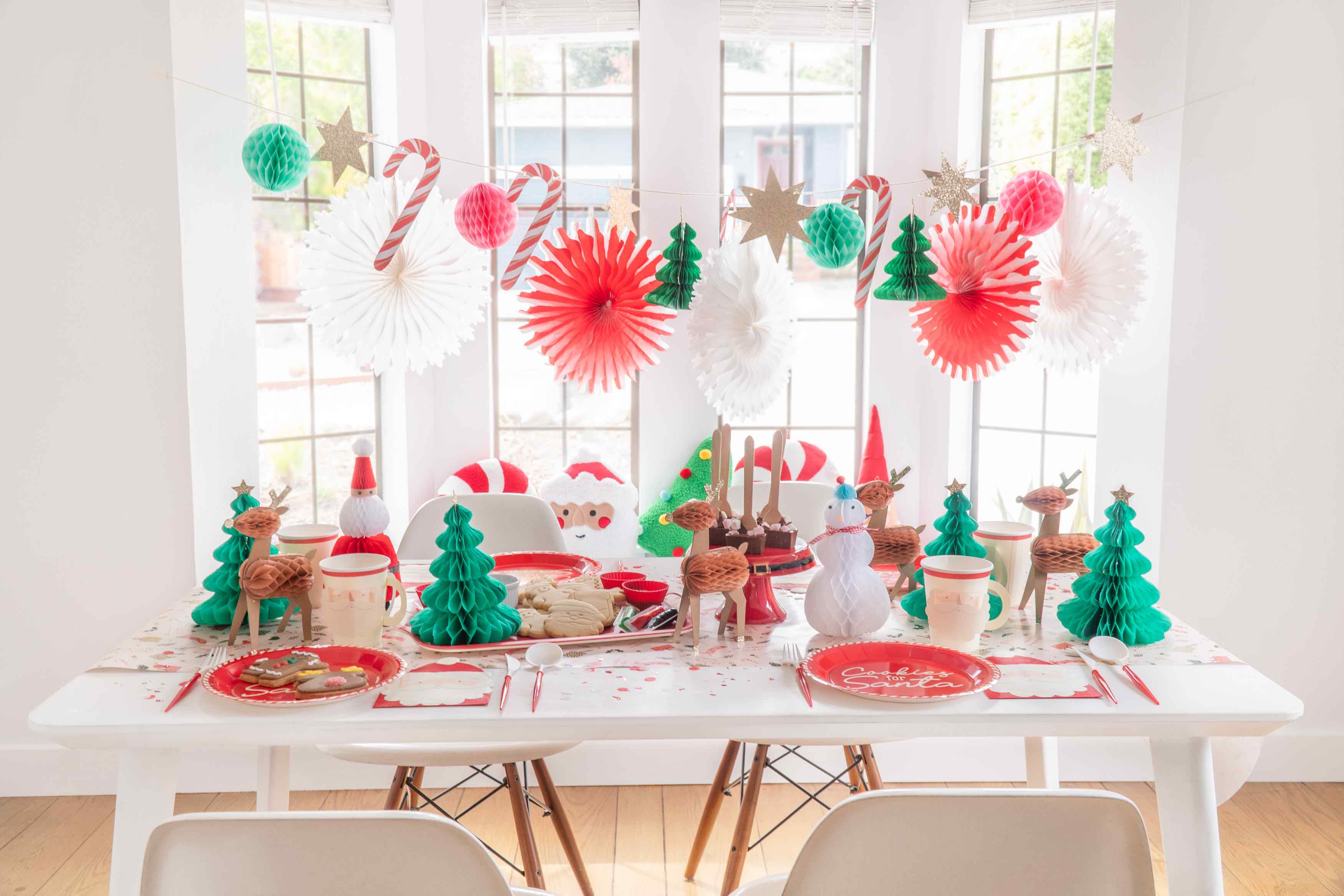 How to host a Christmas cookie decorating party for kids by Momopartys featuring festive Christmas honeycomb garland with candy canes, peppermints, Christmas trees hung next to the windows. On the table are Christmas character honeycombs with Santa.