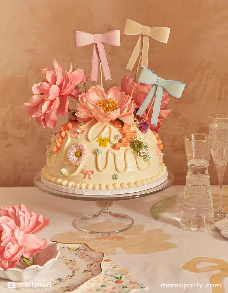 A gorgeous floral cake adorned with beautiful spring flowers and Momopartys's 3D pastel bow toppers. On the table there are Meri Meri's elegant floral plates and napkins.