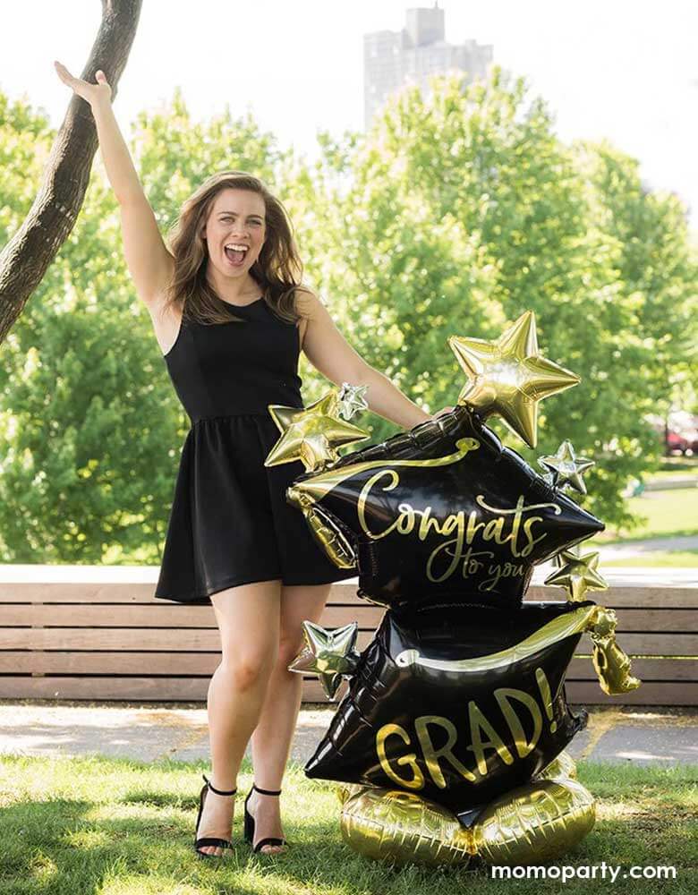 A high school or college graduation standing next to Momopartys's 51" Airloonz Congrats To You Grad Foil Mylar Balloon by Anagram Balloons. Her hand is up in the air celebrating her big achievement on the graduation day.