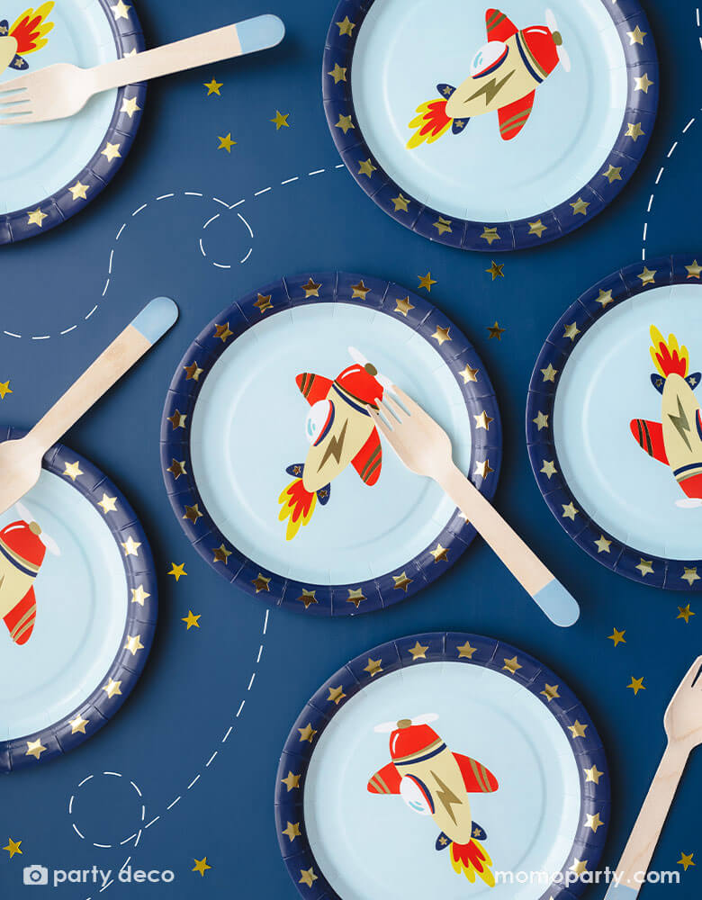 A navy blue table featuring 6 of Momopartys's 7" Airplane Round Paper Plates and blue dipped wooden forks by Party Deco. Featuring gold foil stars around the edge and a vintage cream and red colored airplane design on a blue sky light blue background, this set of 6 round plates are perfect for your kid's plane or aviation themed celebration.