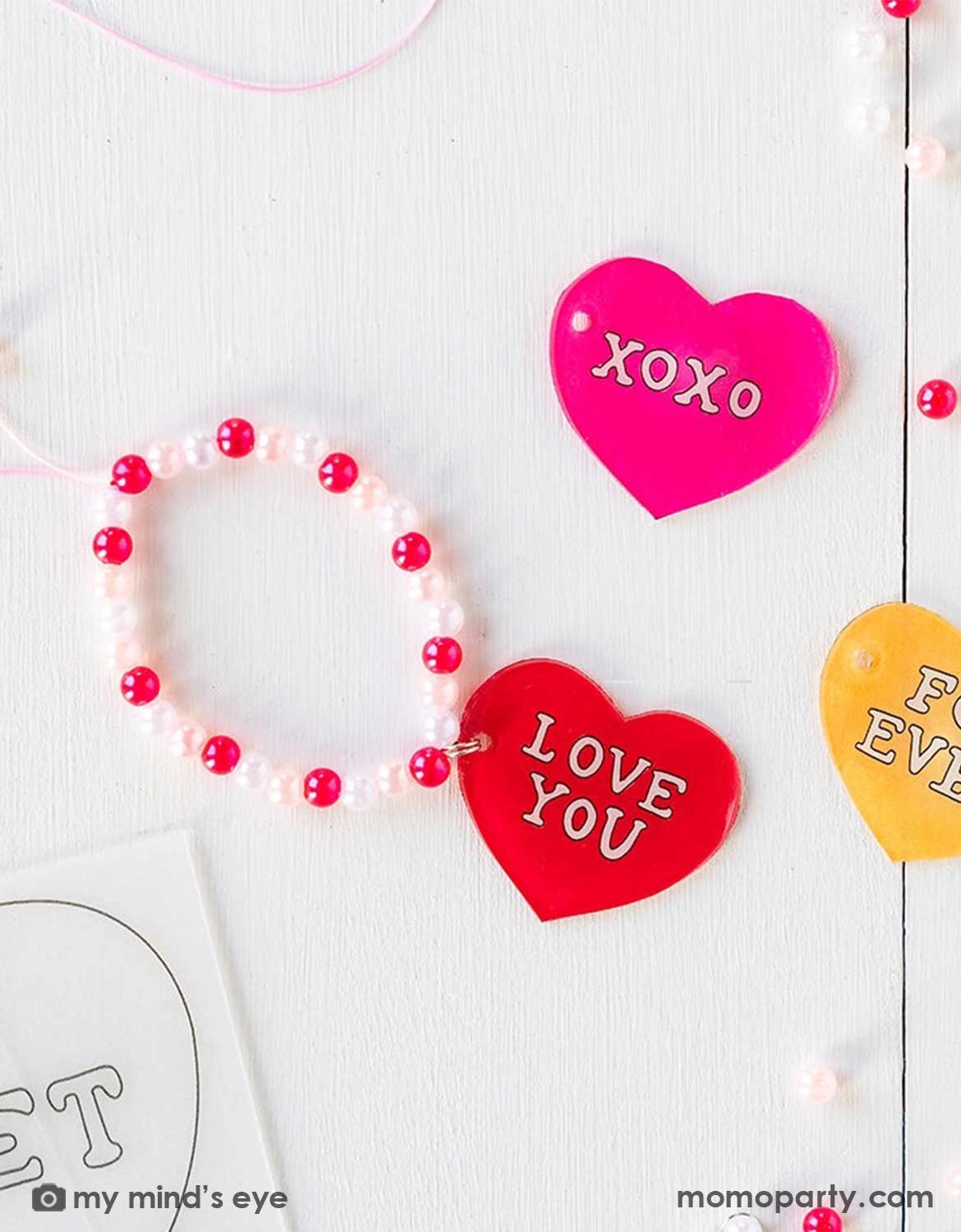 Pink and red heart-shaped bracelet charm with 'LOVE YOU' and 'XOXO' text  and beads on a light background.
