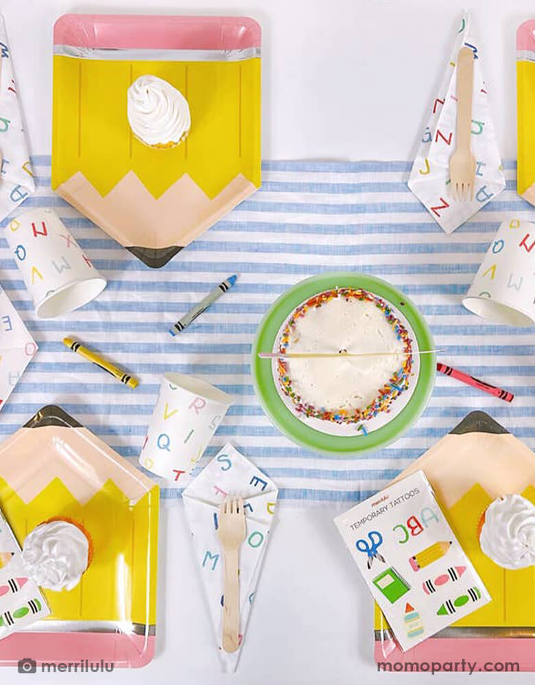 A school themed party table filled with Momopartys's school themed party supplies including a pencil shaped plate, ABC alphabet patterned napkins, plates and cups. Next to the tableware there's a cake topped with a pencil shaped cake topper with "Hello 2nd Grade". On the pencil plate, there's a tattoo sheet featuring colorful school themed designs including crayon, glue bottle, notebook and more. All this makes a great inspo for a back to school party or first day of school celebration.