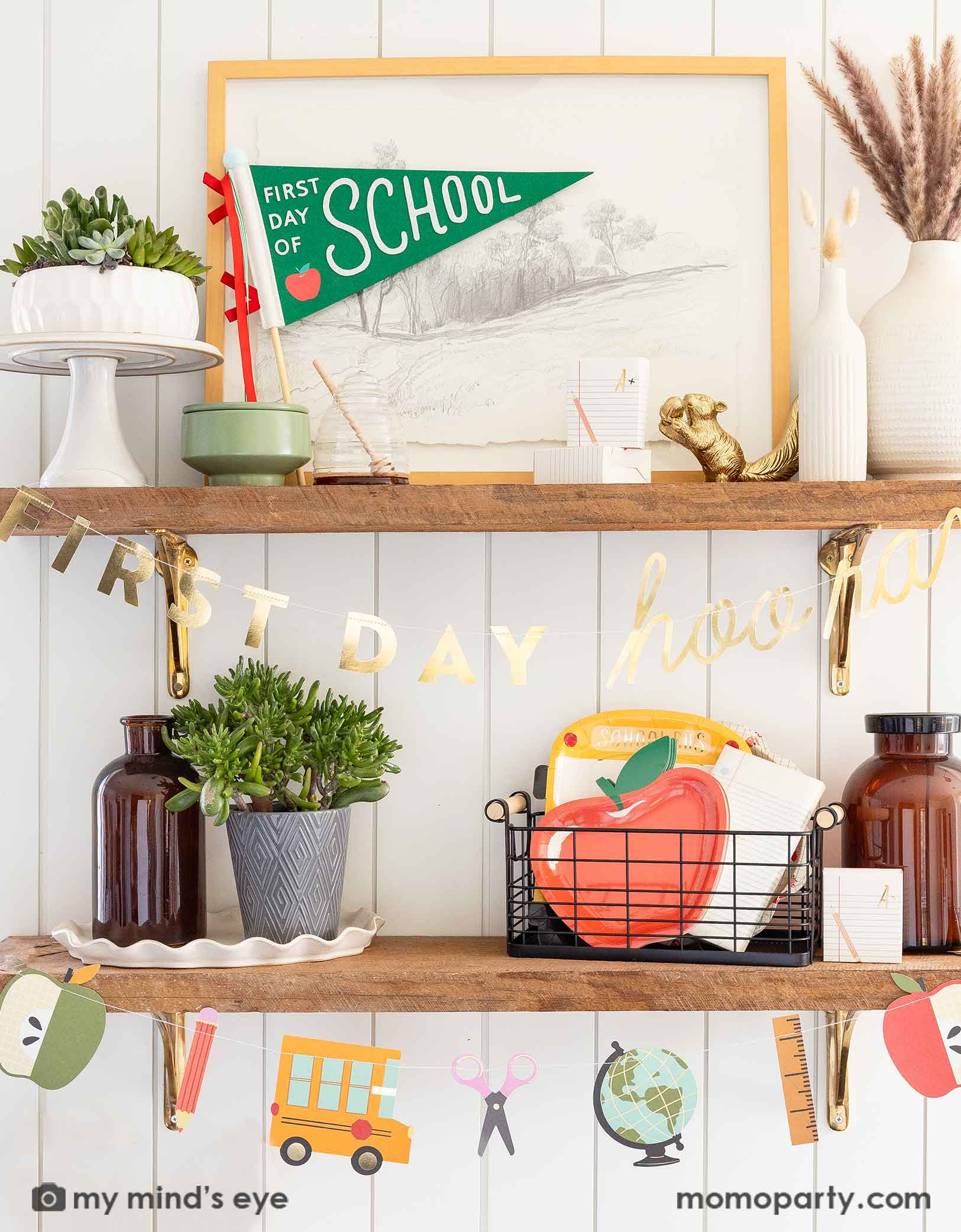 A shelf decorated with various school themed party supplies and decorations from Momopartys including the 'First Day of School' apple party pennant, the first day of school party garland featuring school supply shaped pennants like scissors, rulers, apples, globes and school buses.  On the shelf there is a basket filled with school themed party tablewares including apple shaped plates, school bus shaped plates, notebook napkins. A modern home decoration idea to celebrate kid's first day of school.