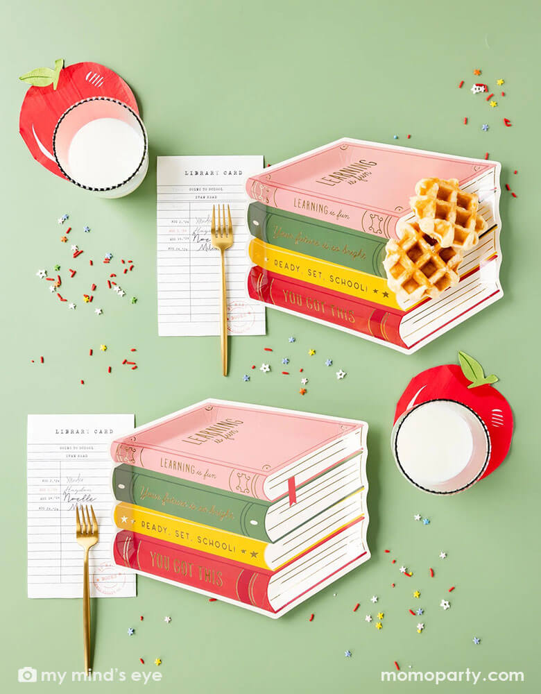 A green table with Momopartys's 11" Stack of Books Shaped Paper Plates, Library Card Shaped Napkins, Apple Shaped napkins by My Mind's Eye. Comes in a set of 8 paper plates, add some literary charm to your back-to-school party with these fun Stack of Books Paper Plates. The whimsical design resembles a stack of books in the color of pink, green, yellow and red, giving a playful touch to your mealtime. These are great for kid's back to school parties or first day of school celebrations.