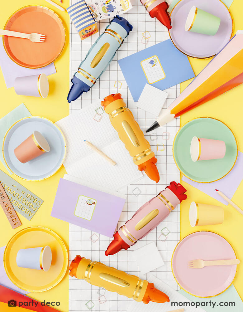 A overhead shot of a back to school party table featuring Momopartys's school themed tableware and decorations including mini crayon shaped balloon set, a black and white grid table runner, pastel colored plates and party cups and a few pastel colored stationary including notebooks, rulers, pencils etc. Making this a modern and adorable inspo for a fun back to school party or first day of school celebration. 
