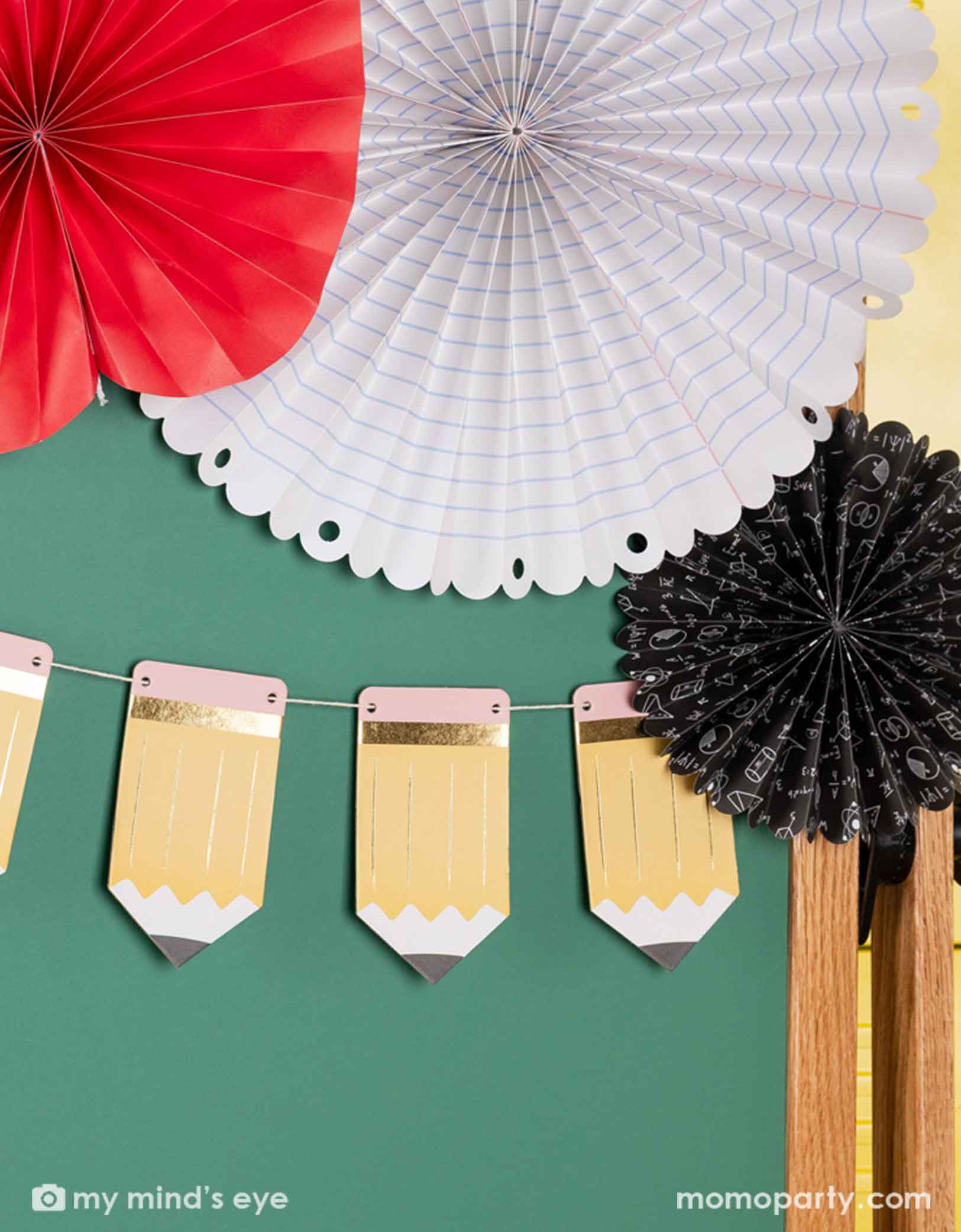 A green chalkboard decorated with the 5' pencil shaped party banner and apple, notebook shaped paper fans from Momopartys. A modern and easy decoration to celebration kid's back to school or first day of school special day.