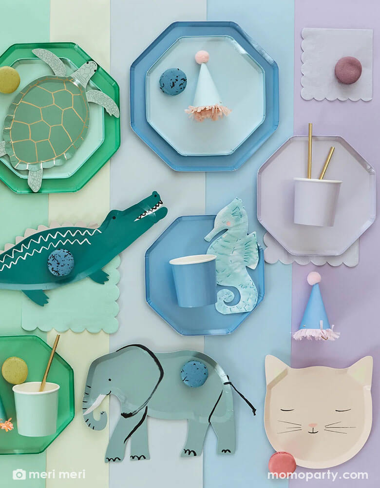A rainbow colored table with party plates, cups, napkins hats and desserts arranged by colors of green, blue and purple. Available at Momopartys, featuring Meri Meri plates, some in die-cut animal shaped including an alligator, a sea turtle, a seahorse, an elephant, a kitty cat, some in basic solid colors, in different sizes, mix and match them to create a happy celebration!