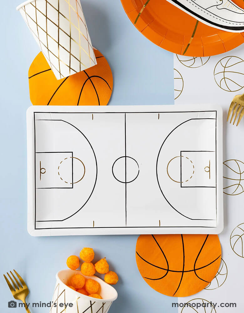 A basketball themed party table features Momopartys's basketball tableware by My Mind's Eye including basketball shaped plates, napkins, basketball court shaped large plates, basketball net gold foil party cups and paper basketball table runner - a perfect table setting inspo for kid's basketball themed birthday parties or a fun NBA viewing party!