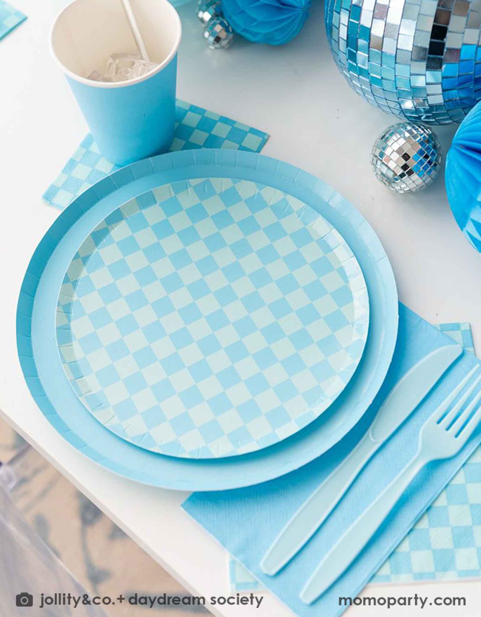 A blue themed party table features Momopartys's Check it! Blue and Blue Checkered Tableware Collection by Jollity & Co. including 10" blue dinner plates, 8" blue checkered dessert plates, 6.5" large napkins, and 5" blue checkered small napkins, blue plastic utensils and solid blue party cups, with blue honeycomb and disco ball decorations as the centerpiece for the party table.