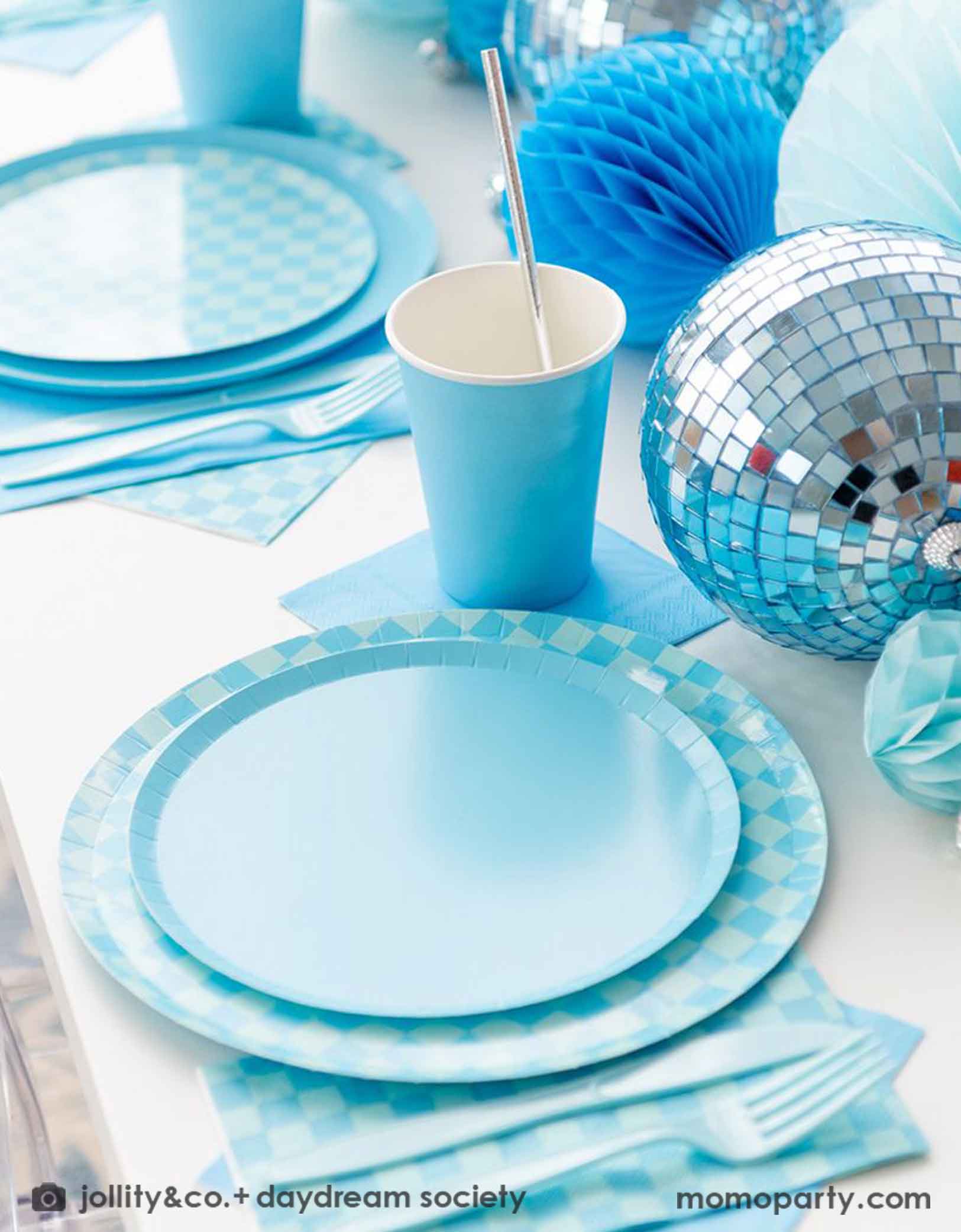 A blue themed party table features Momopartys's Blue and Check it! Blue Checkered Tableware Collection by Jollity & Co. including 10" blue checkered dinner plates, 8" blue dessert plates, 6.5" blue checkered large napkins, blue plastic utensils and solid blue party cups, with blue honeycomb and disco ball decorations as the centerpiece for the party table.