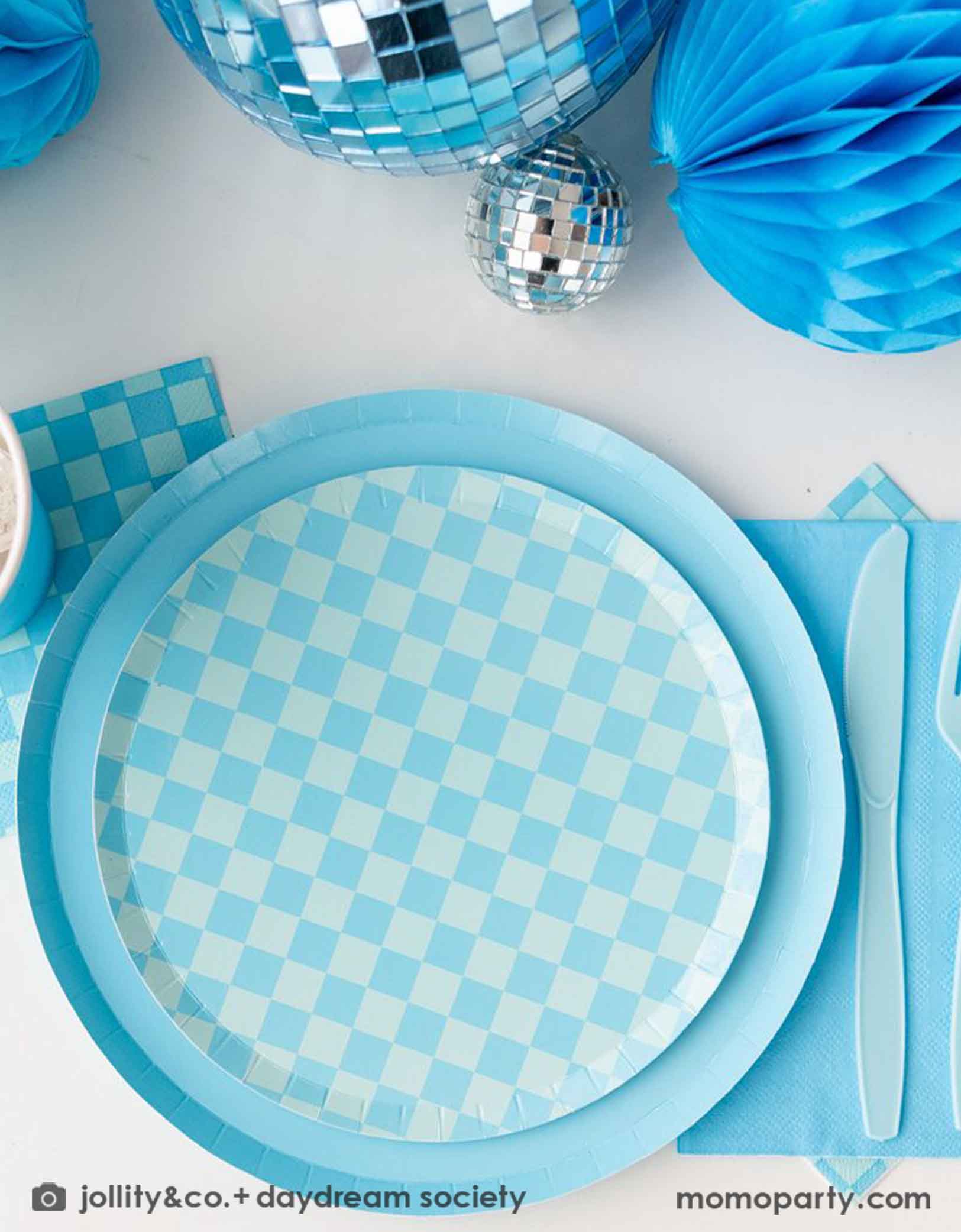 A blue themed party table features Momopartys's Check it! Blue and Blue Checkered Tableware Collection by Jollity & Co. including 10" blue dinner plates, 8" blue checkered dessert plates, 6.5" large napkins, blue plastic utensils and solid blue party cups, with blue honeycomb and disco ball decorations as the centerpiece for the party table.