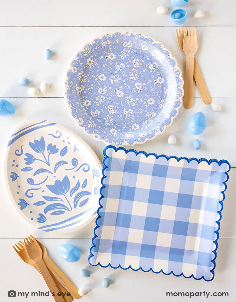 An overhead shot of a beautiful Easter party tablescape featuring Momopartys's Easter themed party supplies in light blue including the floral egg shaped plate, blue ditsy floral scallop plate and the blue gingham large plate, with blue Easter eggs and egg shaped candies spread out - a perfect inspo for an elegant Easter celebration.