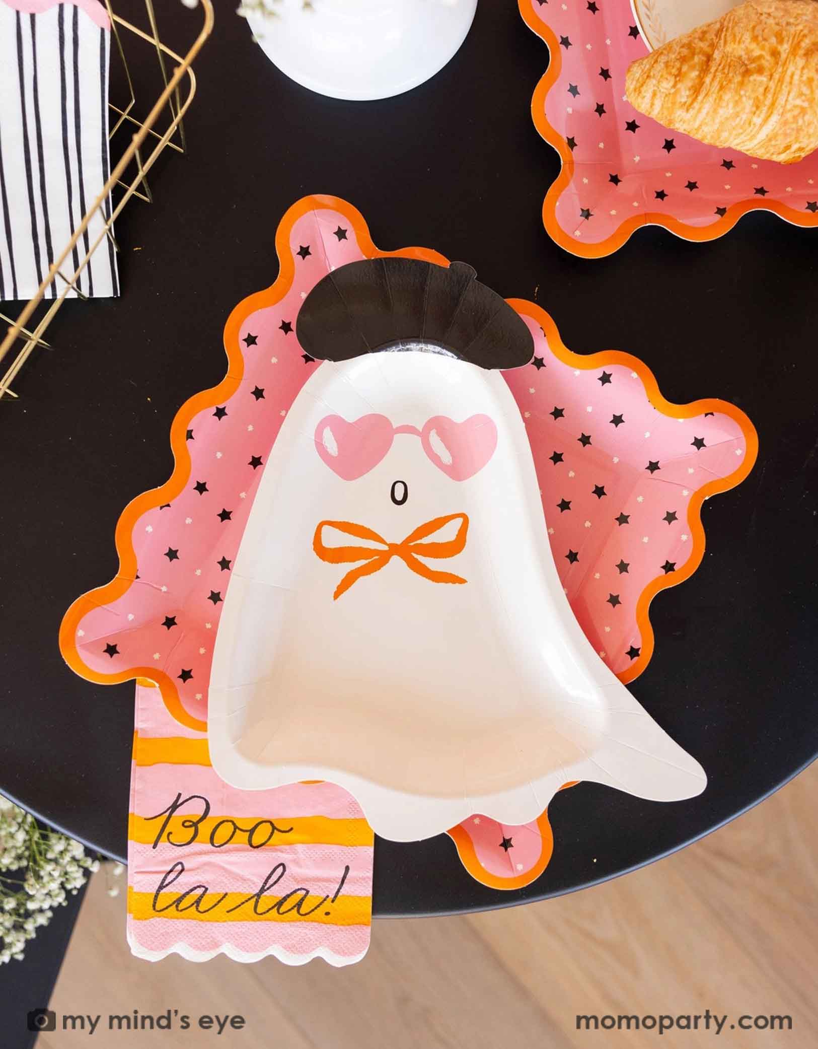 A pink Halloween party table featuring Momopartys's Boo La La ghost themed party tableware by My Mind's Eye including the ghost diecut shaped plate, the pink star striped dinner plates, the orange and pink striped dinner napkin with 'Boo la la!' text. A chic and sweet Halloween party tablescape.