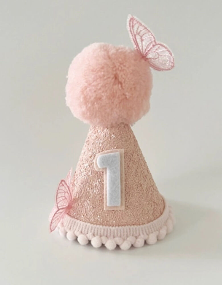Butterfly glitter first birthday hat from momopartys.shop. Adorned with beautiful butterflies on glitter base with darling pom poms at the bottom, this birthday hat adds the perfect touch of cuteness to any party outfit. A must-have for your little girl's first big day.