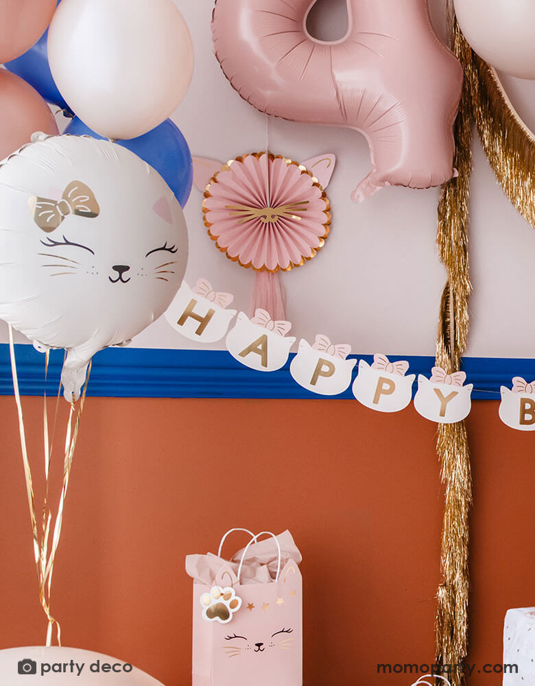 A kid's cat themed birthday party decoration set up features Momopartys's cat themed party supplies by Party Deco including 18" kitty cat shaped foil balloon in cream, along with some latex balloon mix in pink, blush and royal blue. On the wall there are pink kitty cat shaped party fans along with a gold tinsel garland hung on. With a pink number 4 foil balloon and a cat head shaped happy birthday banner, it makes an adorable inspo a cat or pet themed party.