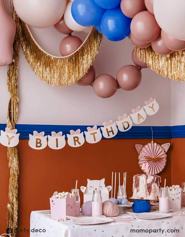 A kid's cat themed birthday party decoration set up features Momopartys's cat themed party supplies by Party Deco including 18" kitty cat shaped foil balloon in cream, along with some latex balloon mix in pink, blush and royal blue. On the wall there are pink kitty cat shaped party fans along with a gold tinsel garland hung on. With a pink number 4 foil balloon and a cat head shaped happy birthday banner, it makes an adorable inspo a cat or pet themed party.