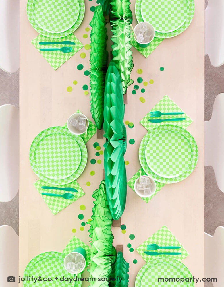 A green themed party table features Momopartys's Check it! Lime Green Checkered Tableware Collection by Jollity & Co. including 10" dinner plates, 8" dessert plates, 6.5" large napkins, green utensils and solid green party cups, with green paper fans as the centerpiece and large round green confetti scattered on the table.