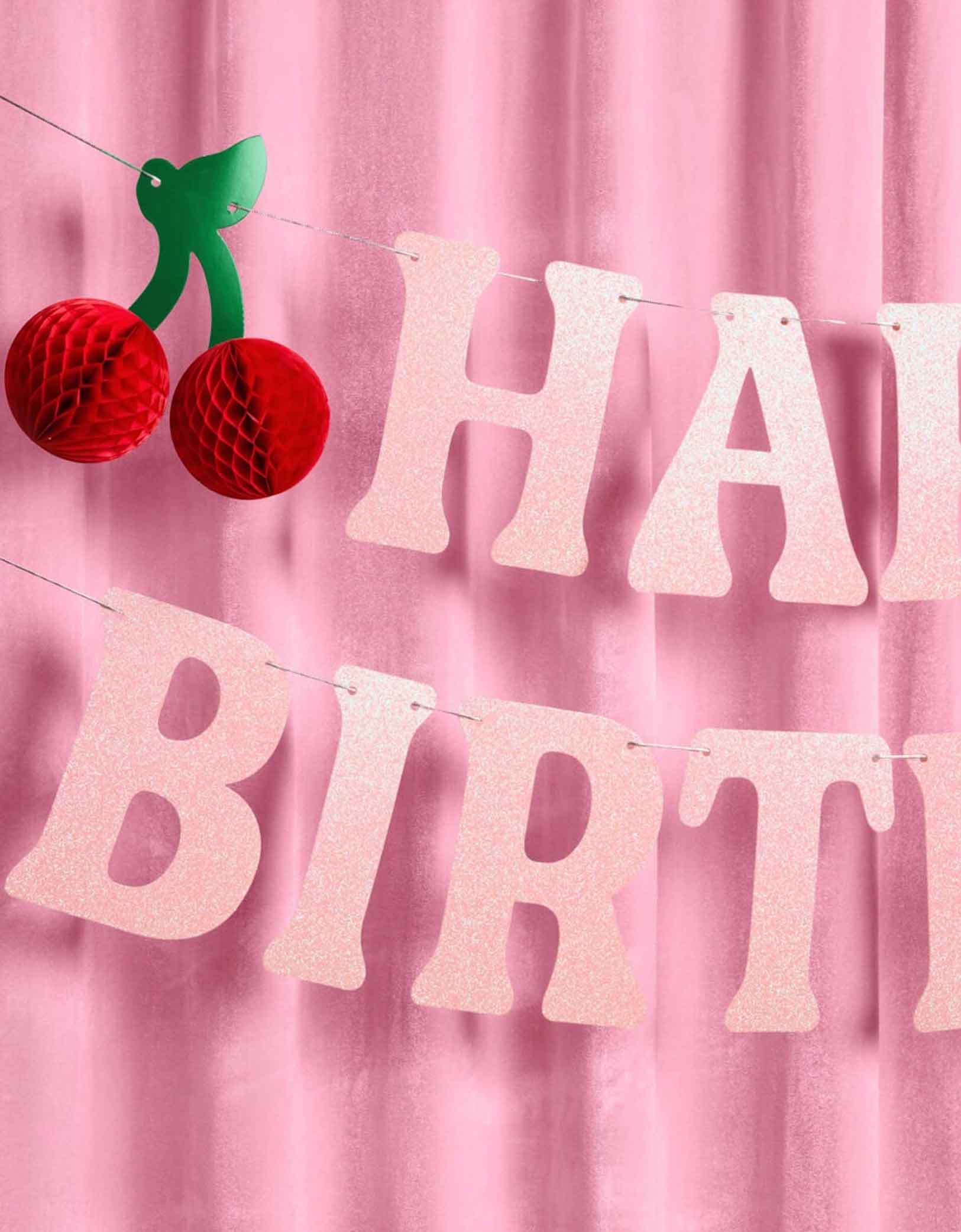 A close up of Momopartys's 4.5' cherry happy birthday banner hung against a pink curtain.