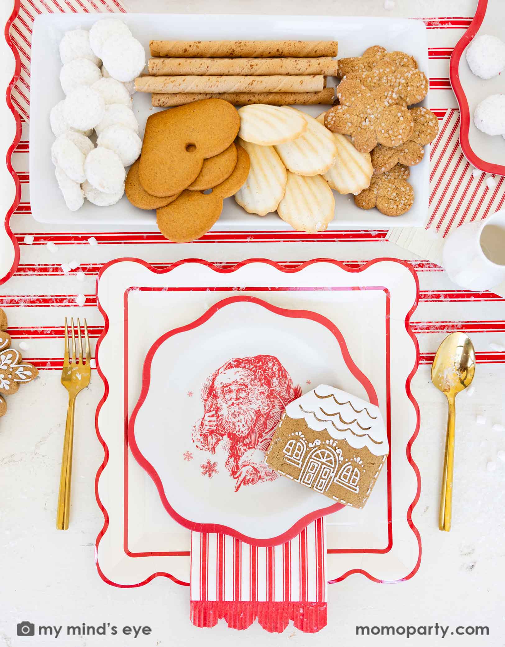 Christmas-themed table place setting with Holiday cookies, crackers, and decorative plates featuring a Santa Claus design, along with red striped scalloped dinner napkins and paper table runner from Momopartys.