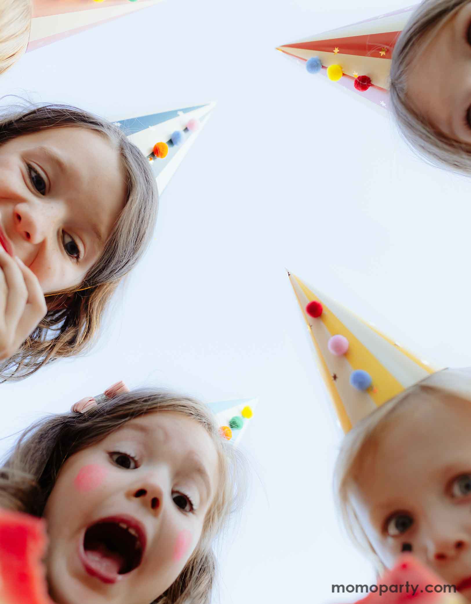 A bunch of kids dressed dressed in the vintage circus outfits and makeup wearing Momopartys's festive colorful party hats with pom poms looking into the camera and making funny faces. This set of 6 party hats features vibrant stripes in 6 different colors and colorful pom poms, adding a touch of carnival magic to any event.