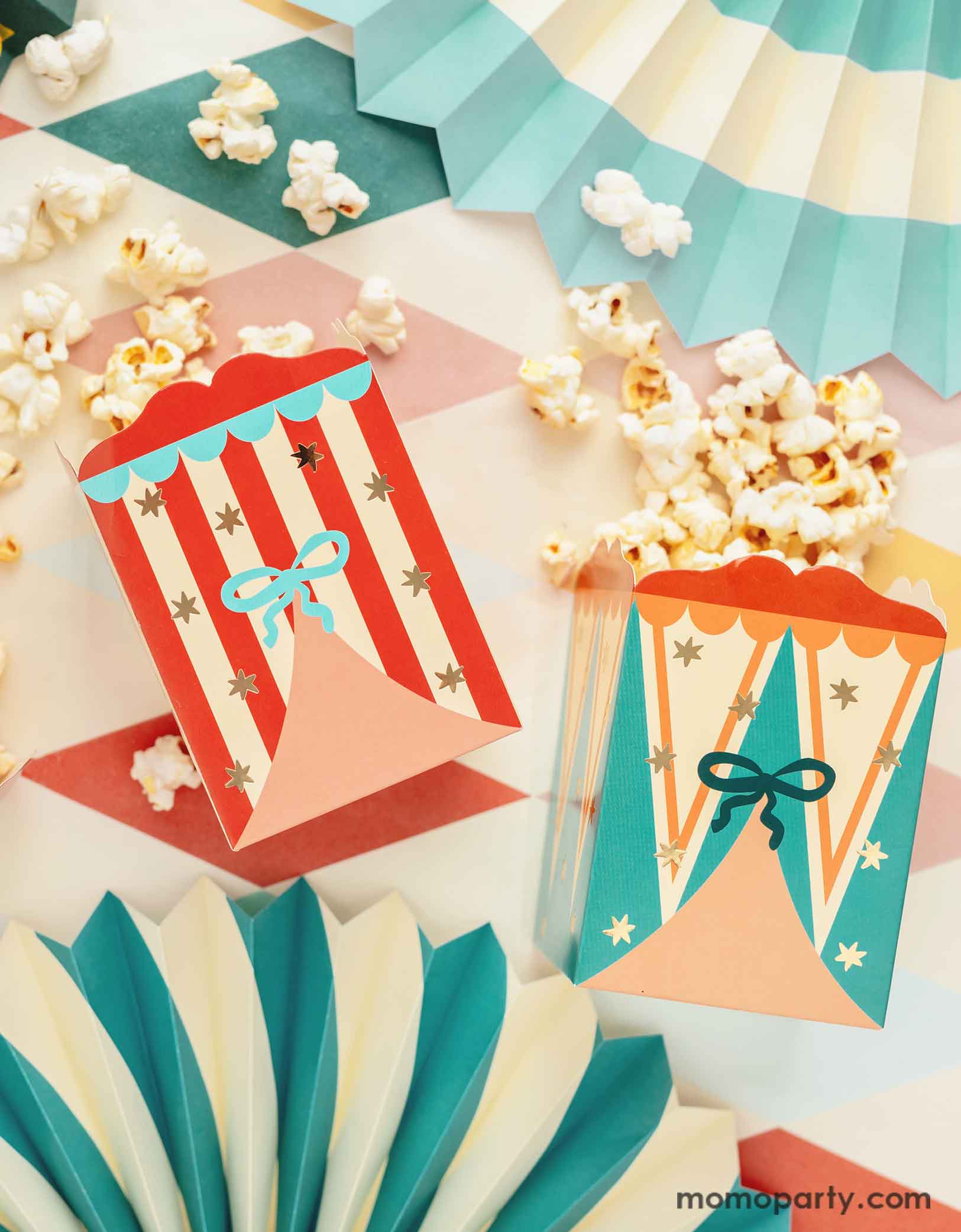 A carnival/circus themed part table featuring Momopartys's circus themed party supplies including  the festive treat boxes filled with popcorn and colorful paper fans on a circus themed striped table cover - making this great table setting idea for a fun and festive kid's carnival themed birthday celebration!