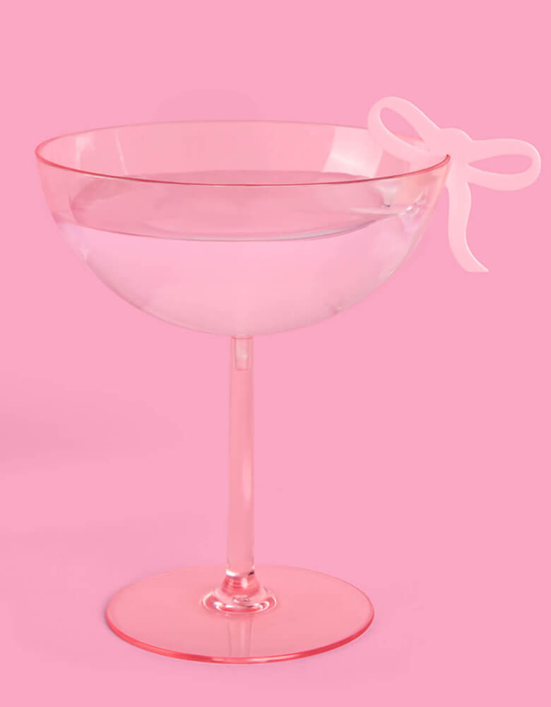 A pink cocktail glass adorned with Momopartys's coquette bow drink marker by Xo, Fetti. Whether it's a bday, bridal shower, or a bachelorette party, celebrate in bow bliss with this super cute drink marker.