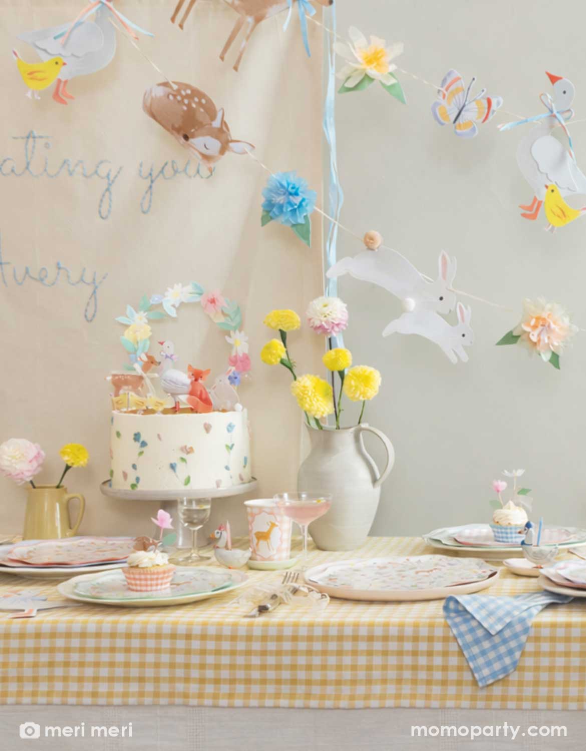 A rustic cottage themed table setting with little woodland animals of deer, goose, bunny, fox, chicks in tablewares and decorations from Momopartys - including floral little animal cake toppers, party cups, matching plates and napkins and an adorable party garland hung above the table covered with a soft gingham tablecloth. With spring florals in soft yellow and pink on the table, this table is perfect for a baby shower, an Easter celebration or young kid's storybook rustic cottage inspired birthdays. 