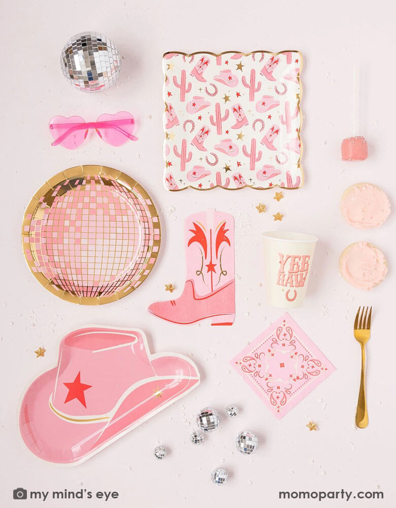 A cowgirl rodeo Western themed party table features pink cowgirl themed party supplies from Momopartys including pink cowgirl boot shaped napkins, cowgirl hat shaped plates, pink disco ball shaped plates, pink bandana small napkins, yeehaw party cups and cowgirl pattern paper plates by My Mind's Eye, along with festive disco ball decorations, heart shaped sunglasses and pink treats, this makes a perfect inspo for kid's cowgirl themed birthday party or a disco cowgirl bachelorette party celebration!