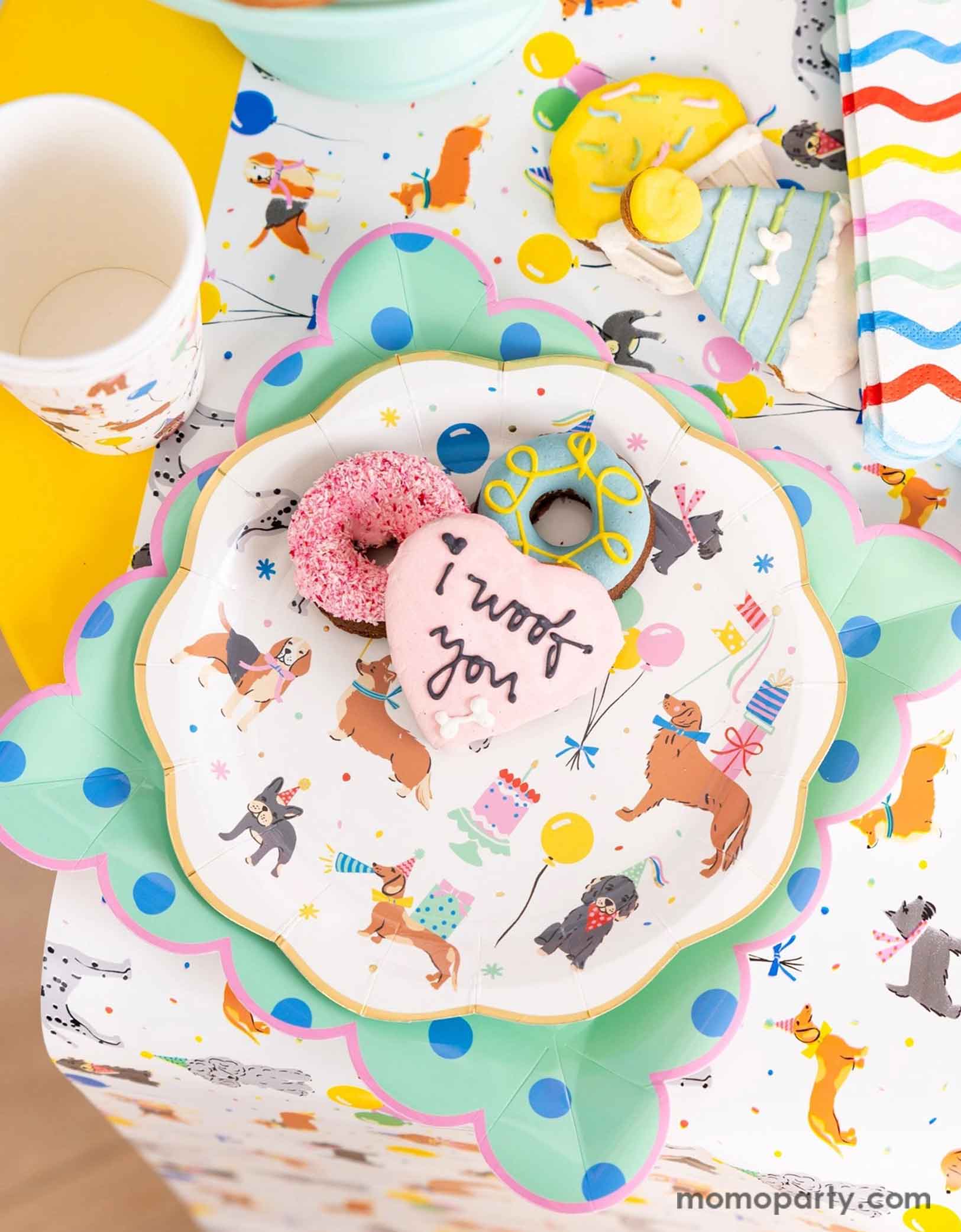A festive and cheerful dog themed party table featuring Momopartys's dog party tableware collection including dog paper plates, party cups, napkins and table runner featuring adorable illustrations of different breeds of dogs with party hats, balloons and birthday cakes. With mint polka dot square plates and birthday festive sugar coated cookies that say "I Woof You" this  table is ready for a fun and playful birthday celebration for a pet lover!