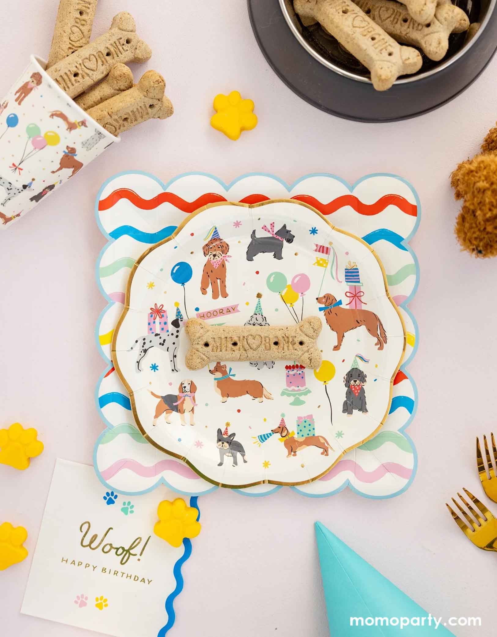 A festive and cheerful dog themed party table featuring Momopartys's dog party tableware collection including the dog paper plate paired with ric rac scalloped square plate, the dog party party cup, and woof napkins. With dog bone cookie treats around, this table is ready for a fun and playful birthday celebration for a pet lover!