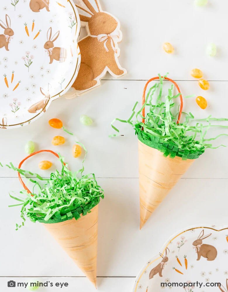 An Easter table features Momopartys's two carrot shaped treat bags by My Mind's Eye filled with Easter colored jelly beans. Around them are 10" x 10" brown rabbit scatter scallop plates and rabbit shaped napkins, makes this a great inspo for an adorable Easter table setting this spring.