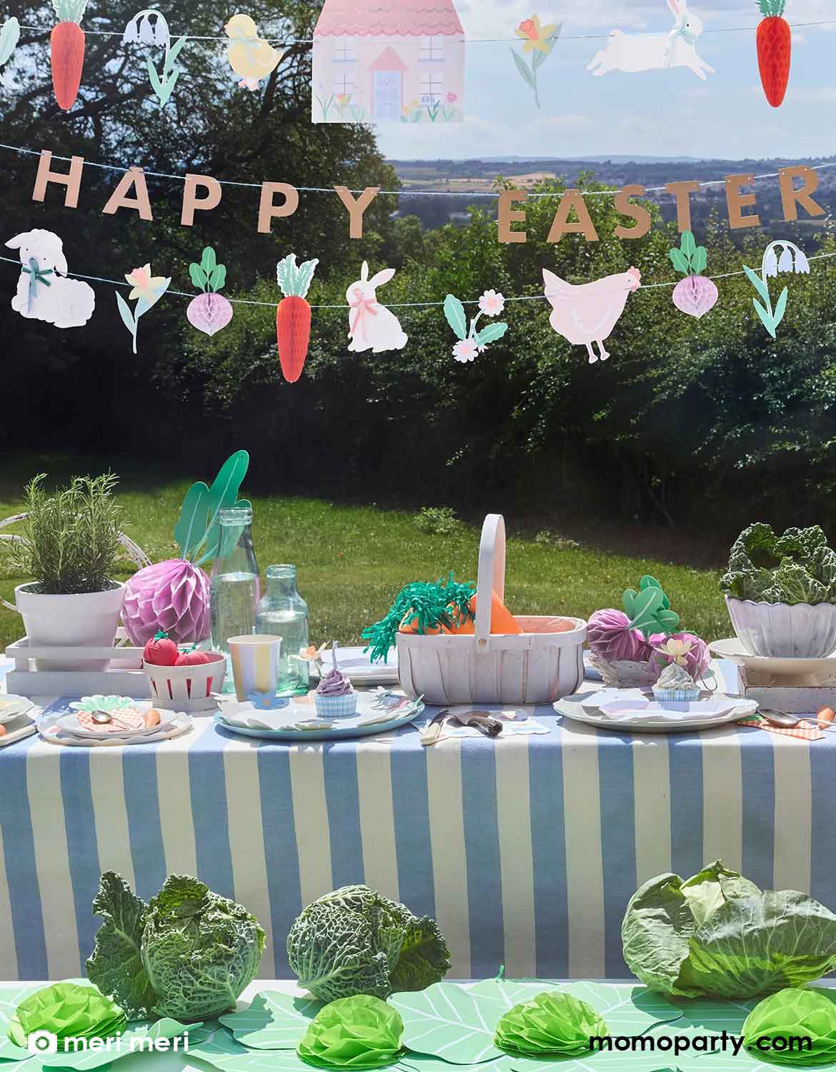 A kid's Easter-themed outdoor table setting with Meri Meri's 'Happy Easter' honeycomb banner and decorative elements hung above. On the table there are various Easter themed tableware and garden vegetable honeycombs including carrots, beets, and lettuces around, making it an adorable set up for kid's Easter celebration or garden themed birthday party in the spring time.  