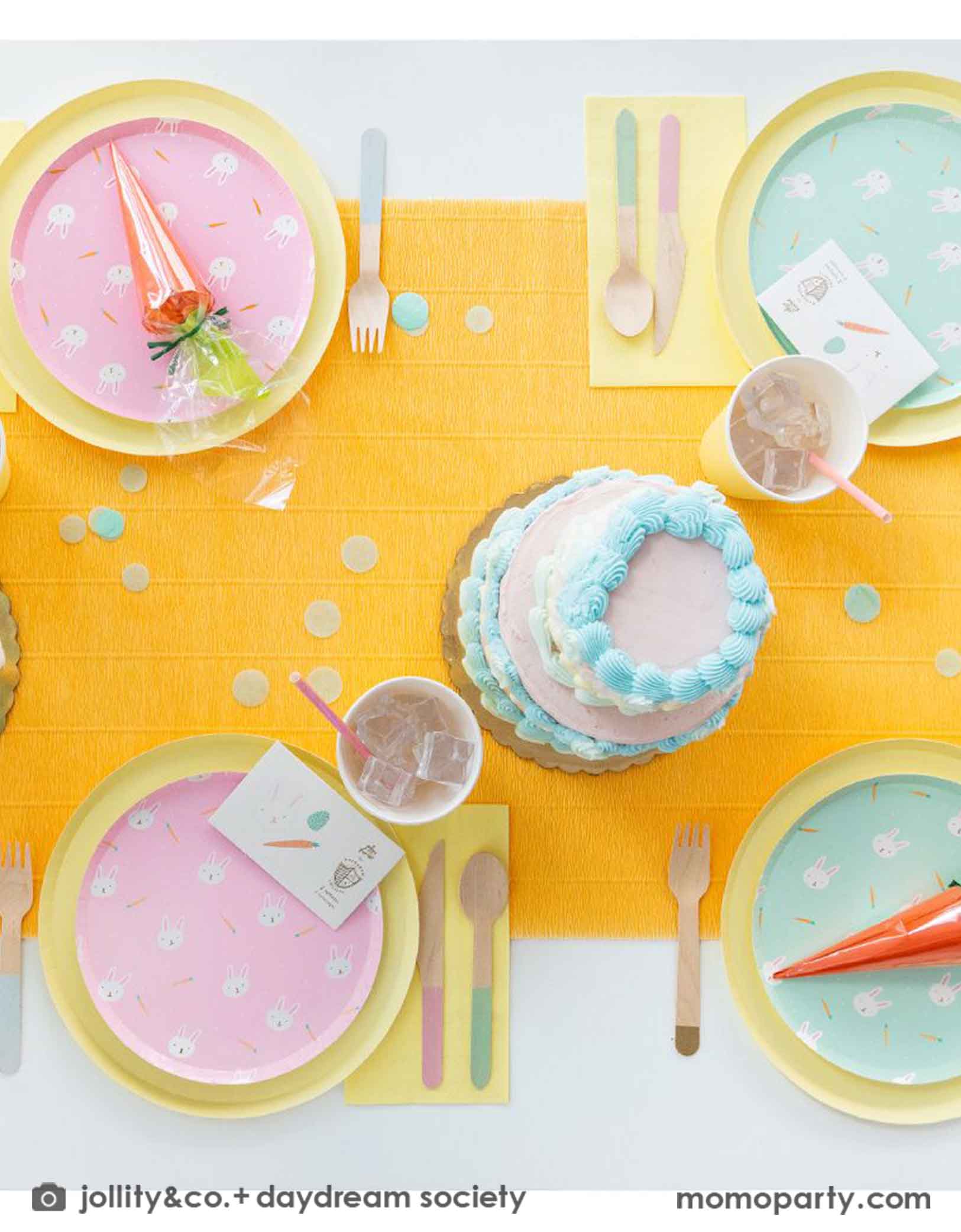A kid's Easter party table featuring Momopartys's Easter Fun party collection by Daydream Society including Easter Fun plates in mint and pink, Easter Fun temporary tattoos, pale yellow dinner plates and party cups. On the table there are two vintage inspired buttercream cakes with pastel piping, making this a perfect inspiration for Easter brunch hosting occasion!