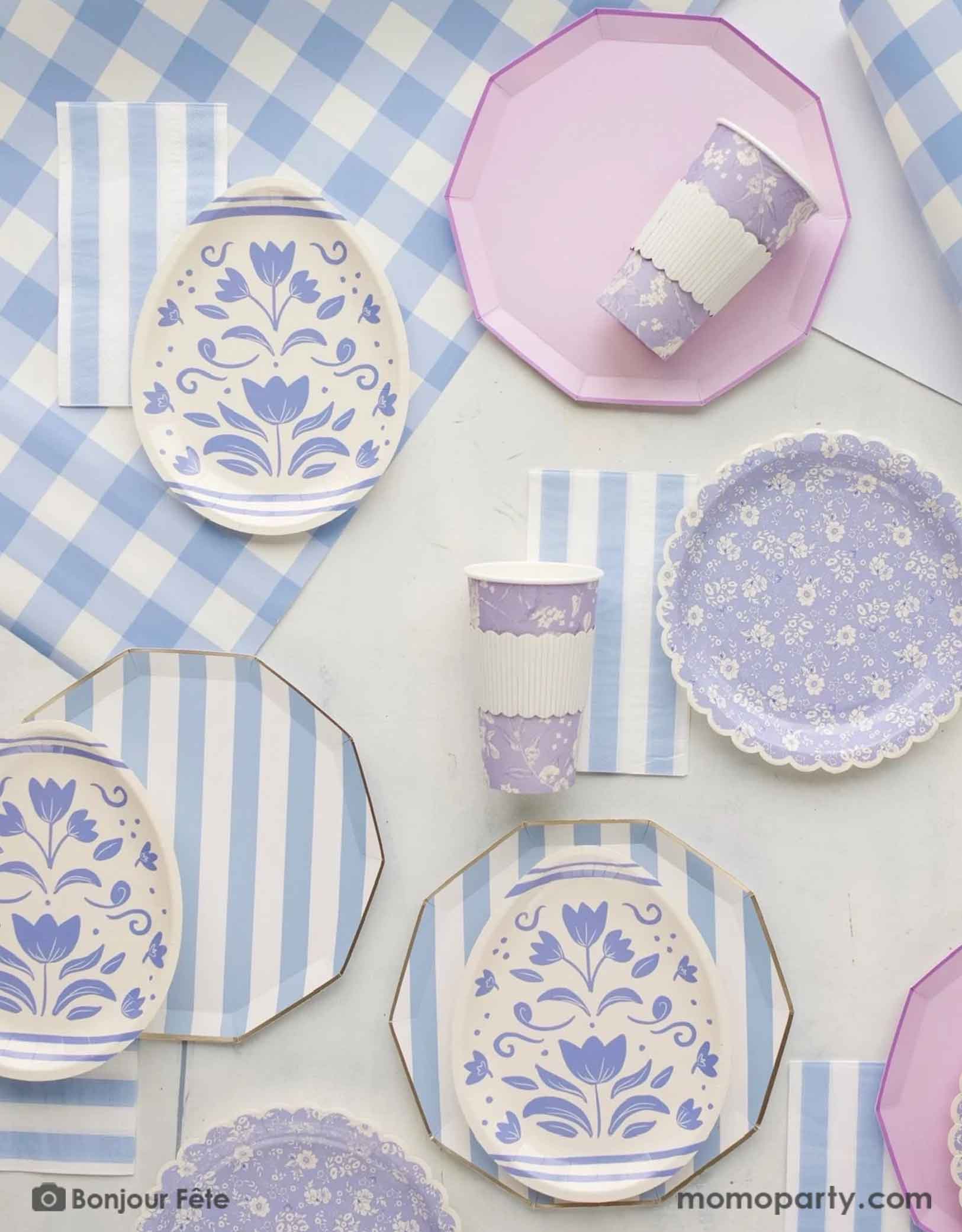 A beautiful Easter party tablescape featuring Momopartys's Easter themed party supplies in light blue and lilac including sky blue cabana striped dinner plates, napkins, floral egg shaped plates, blue ditsy floral scallop plates, matching paper cups on n a blue gingham table runner - the perfect party essentials for an elegant Easter celebration.