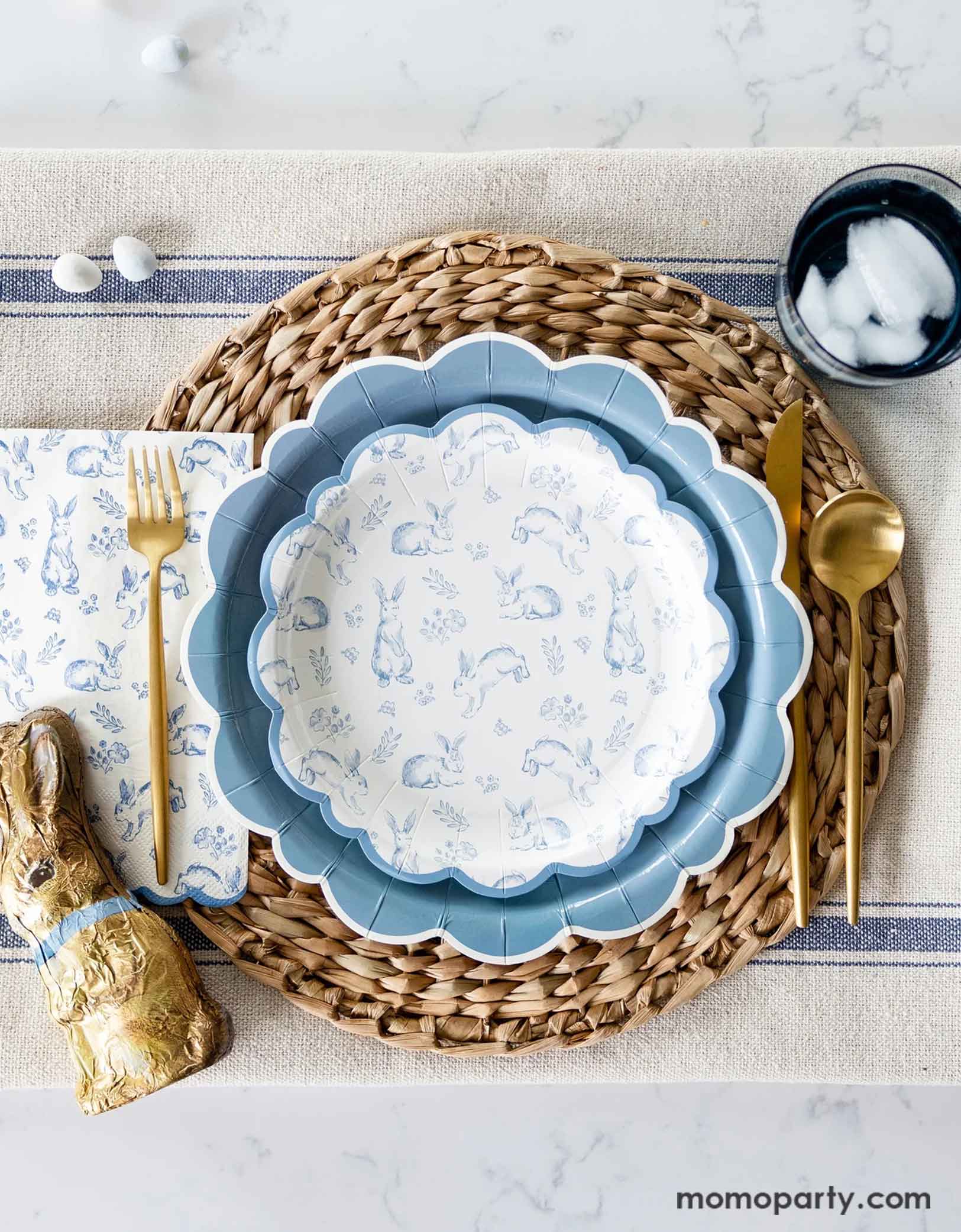 An elegant Easter tablescape with a clean marble table featuring Momopartys's Bunny Toile Collection including The Blue Scalloped Plate, the Bunny Toile Plate and the Bunny Toile Guest Towel by My Mind's Eye. With the gold cutlery set and chocolate bunny and easter egg candies around, this makes great inspiration for a modern and elegant placeset for a Easter gathering this spring season. 