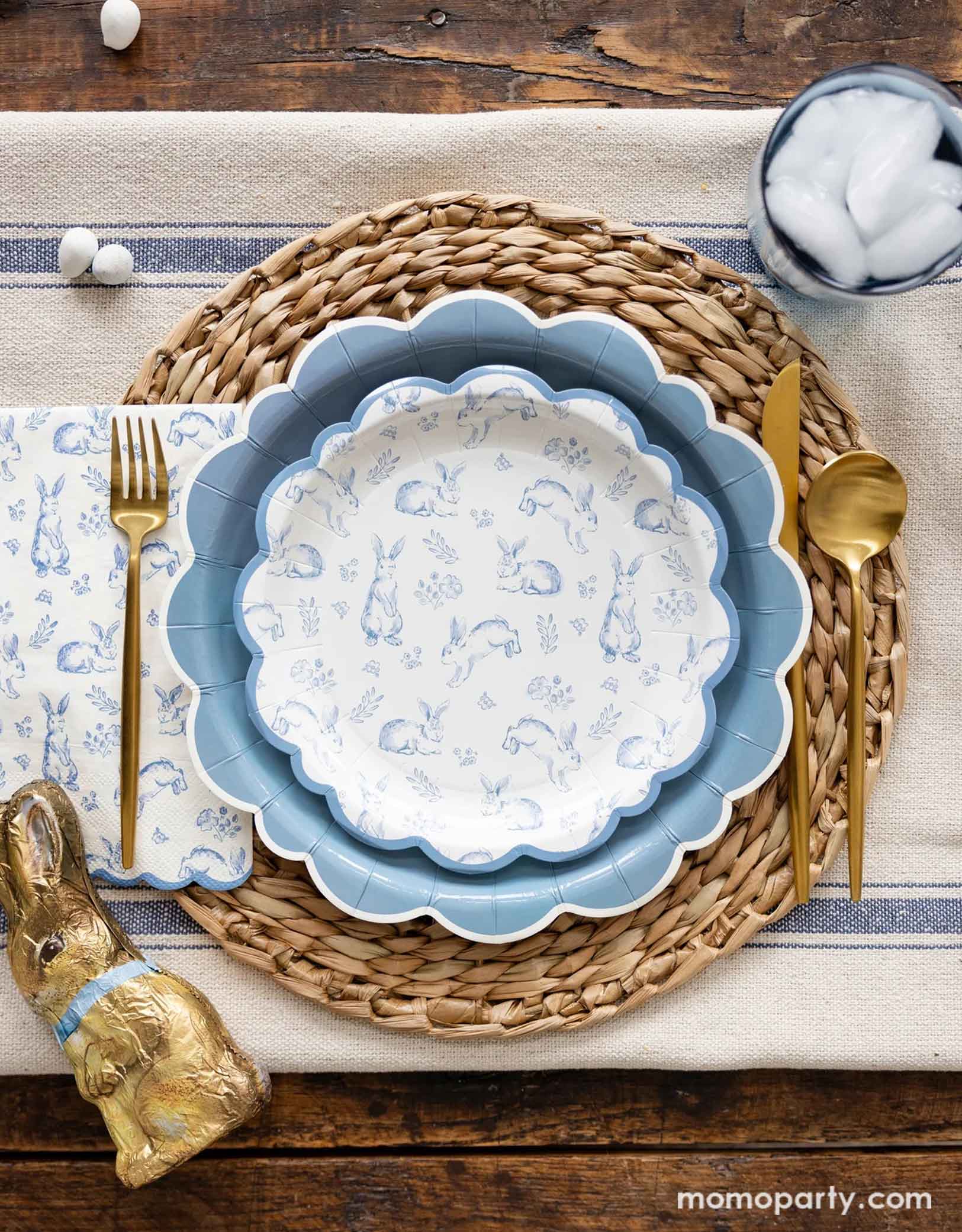 An elegant Easter tablescape with a rustic styled background featuring Momopartys's Bunny Toile Collection including The Blue Scalloped Plate, the Bunny Toile Plate and the Bunny Toile Guest Towel by My Mind's Eye. With the gold cutlery set and chocolate bunny and easter egg candies around, this makes great inspiration for a modern and elegant placeset for a Easter gathering this spring season. 