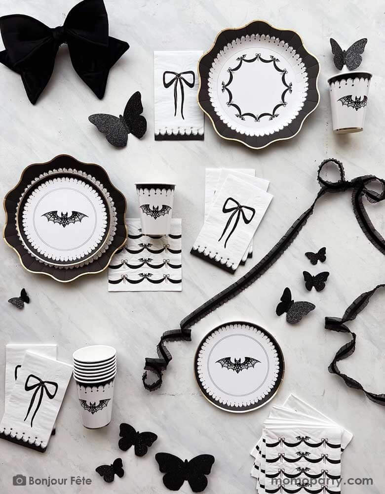 A chic Halloween party tablescape featuring elegant black and white Halloween party supplies with black bow accents from Momopartys, including party plates, cups, napkins and wall decorations. Perfect for a sophisticated Halloween bash for adults in this spooktacular season.