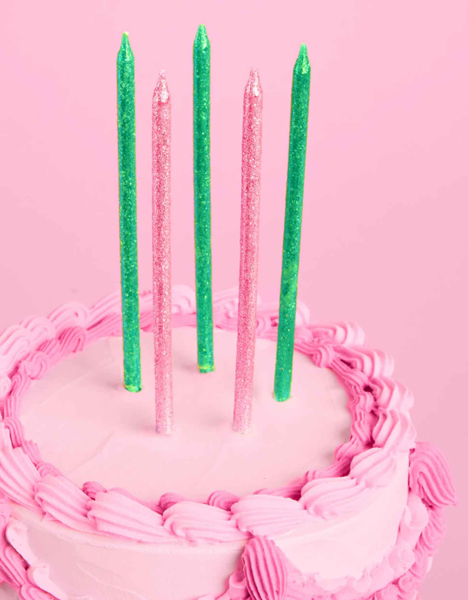 A pink buttercream cake with Momopartys's Wicked Party Emerald City Glitter Candles in pink and green by Xo, Fetti on a pink background.