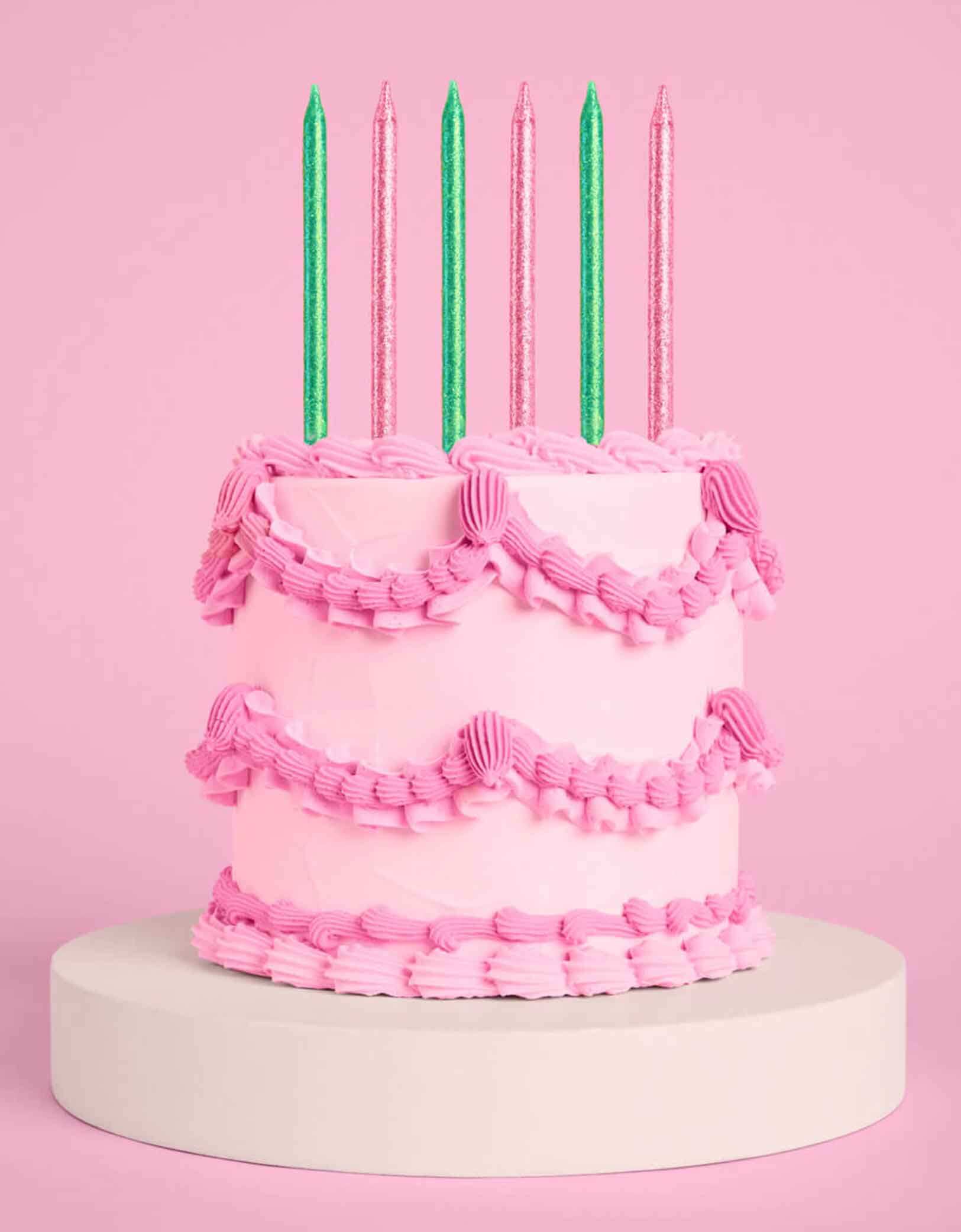 A pink buttercream cake with Momopartys's Wicked Party Emerald City Glitter Candles in pink and green by Xo, Fetti on a pink background.
