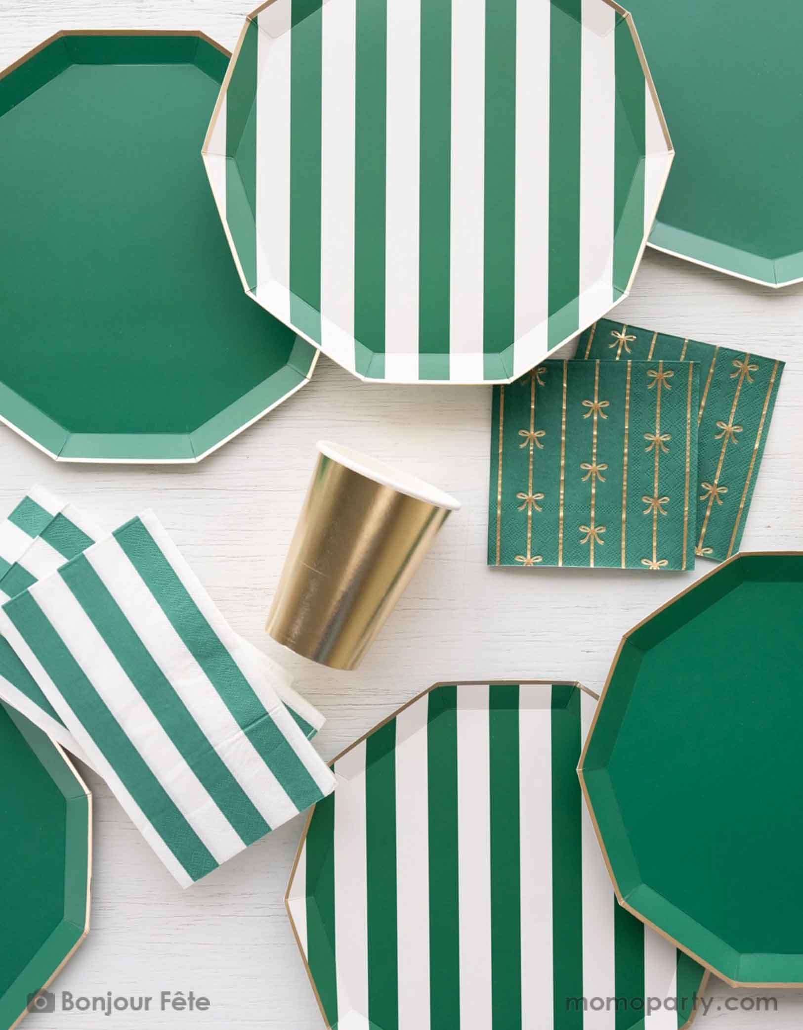 A overhead shot of a party table featuring Momopartys's emerald green and cabana stripe tableware including plates and napkins. With the gold foil bow small napkins and the gold party cup, it brings an elegant touch to your gathering, whether it's a Christmas dinner, a jungle or dinosaur themed birthday party, a football or Super Bowl celebration.